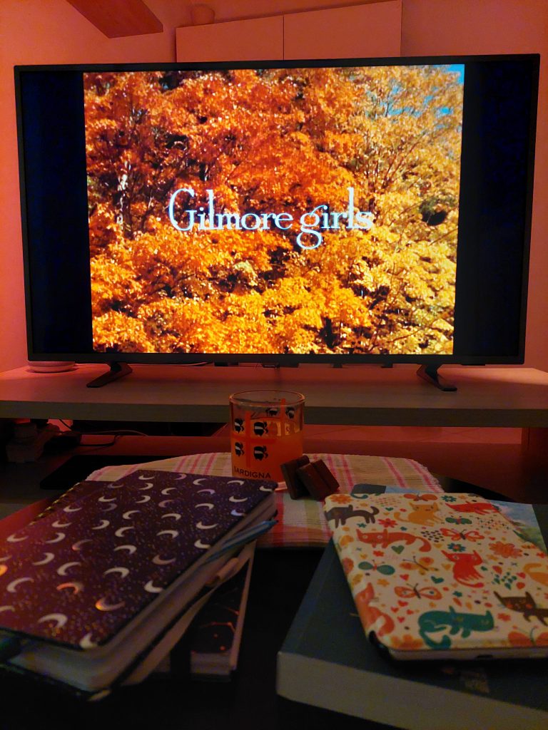 Di cose d'autunno: momento coccola con Gilmore Girls, libri, quaderni, divano e copertina.